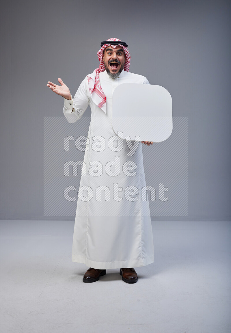 Saudi man Wearing Thob and red Shomag standing holding social media sign on Gray background