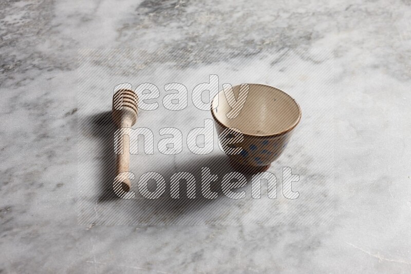 Decorative pottery bowl with wooden honey dipper on the side on grey marble background
