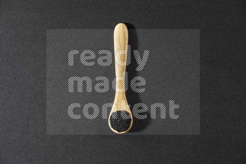 A wooden spoon full of black seeds on a black flooring