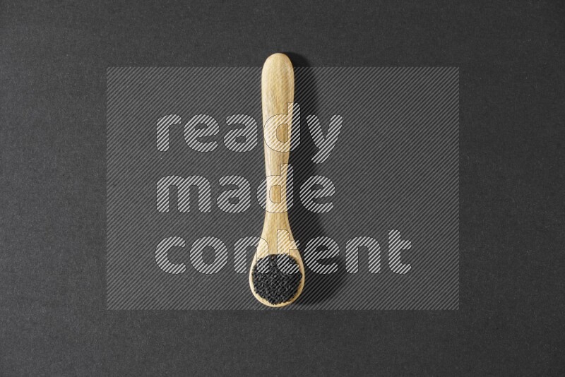 A wooden spoon full of black seeds on a black flooring