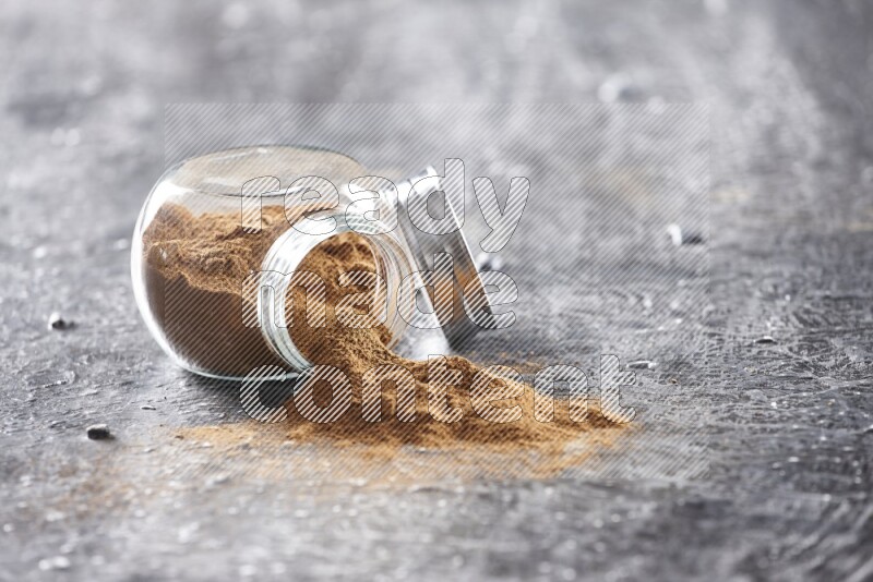 Flipped herbal glass jar full of cinnamon powder on textured black background