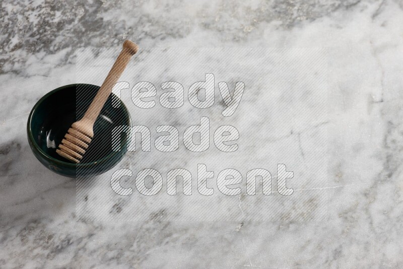 Dark green pottery bowl with wooden honey dipper in it on grey marble background