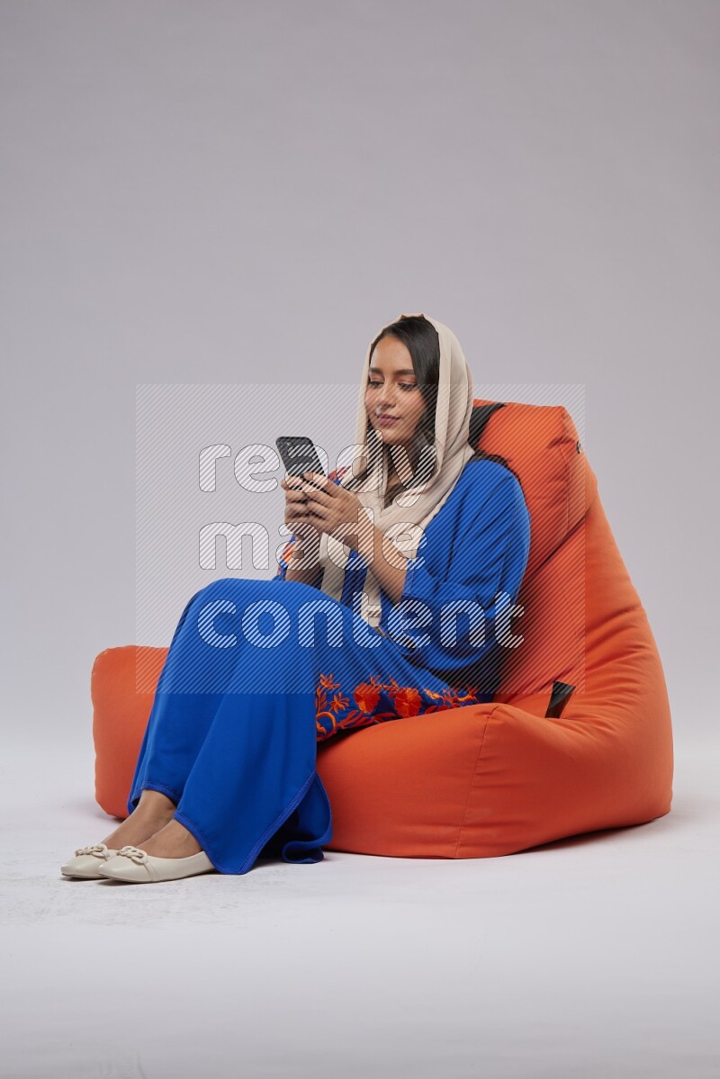 A Saudi woman sitting on an orange beanbag and texting on phone