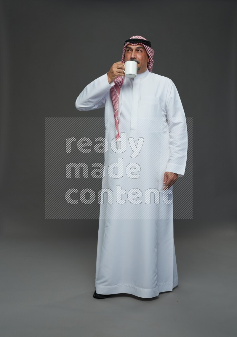 Saudi man with shomag Standing holding mug on gray background