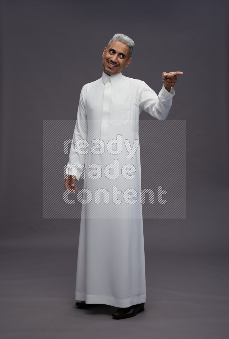 Saudi man wearing thob standing interacting with the camera on gray background