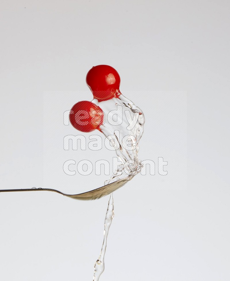 A metal spoon throwing two cherry tomatoes leaving a splash of water behind on a light blue background