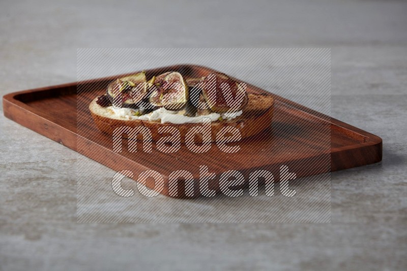 figs halves with cream cheese on toasted sourdough slice on a wooden board on textured grey background