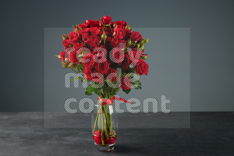 مجموعة من الورود الحمراء الزاهية المربوطة بإحكام بشريط أحمر في مزهرية زجاجية على خلفية من الرخام الأسود