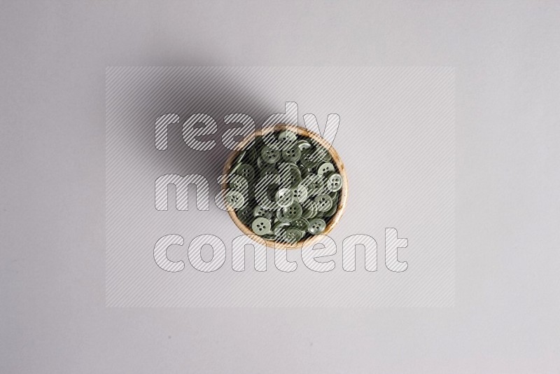 A beige pottery bowl full of colored buttons on grey background