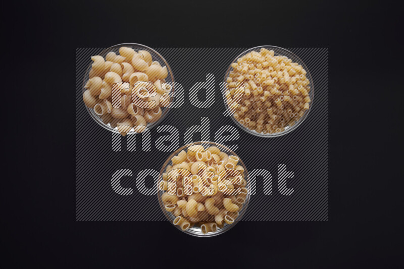 Different pasta types in glass bowls on black background