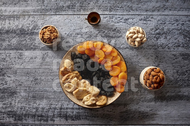 Dried fruits in a pottery plate with nuts and coffee in a dark setup