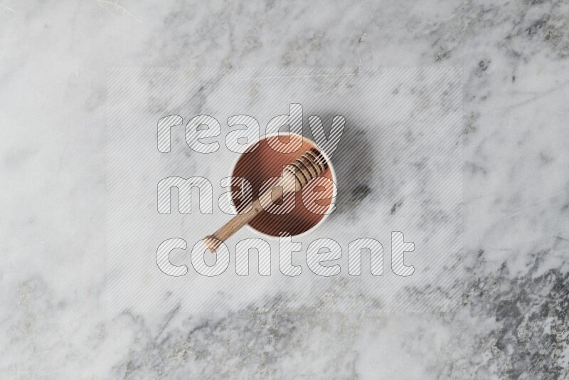 Multicolored pottery bowl with wooden honey dipper in it on grey marble background