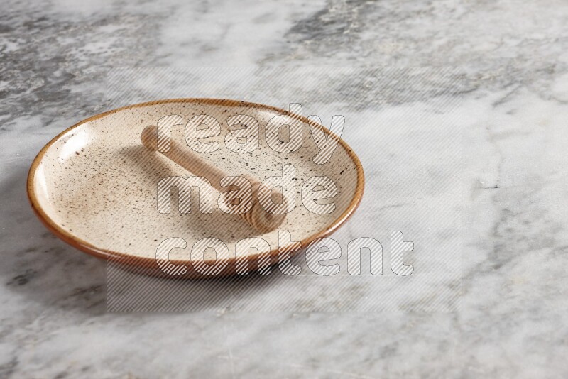 Beige pottery plate with wooden honey dipper in it on grey marble background
