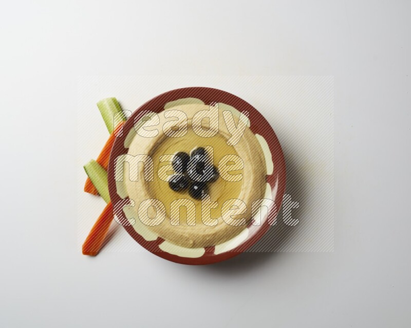 Hummus in a traditional plate garnished with black olives on a white background
