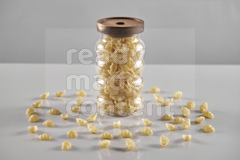 Raw pasta in a glass jar on light grey background