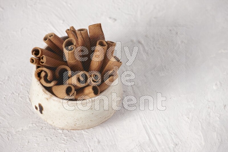 Cinnamon sticks in a beige bowl on a white background