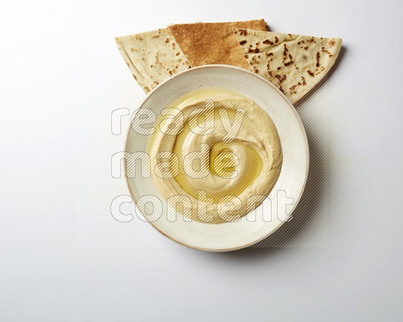 Hummus in a pottry plate garnished with olive oil on a white background