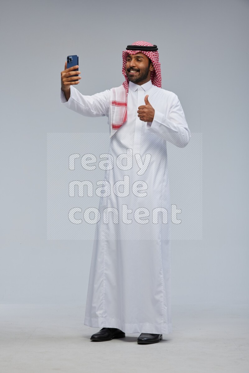 Saudi man Wearing Thob and shomag standing taking selfie on Gray background