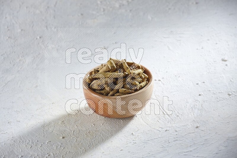 A wooden bowl full of dried turmeric whole fingers on a textured white flooring