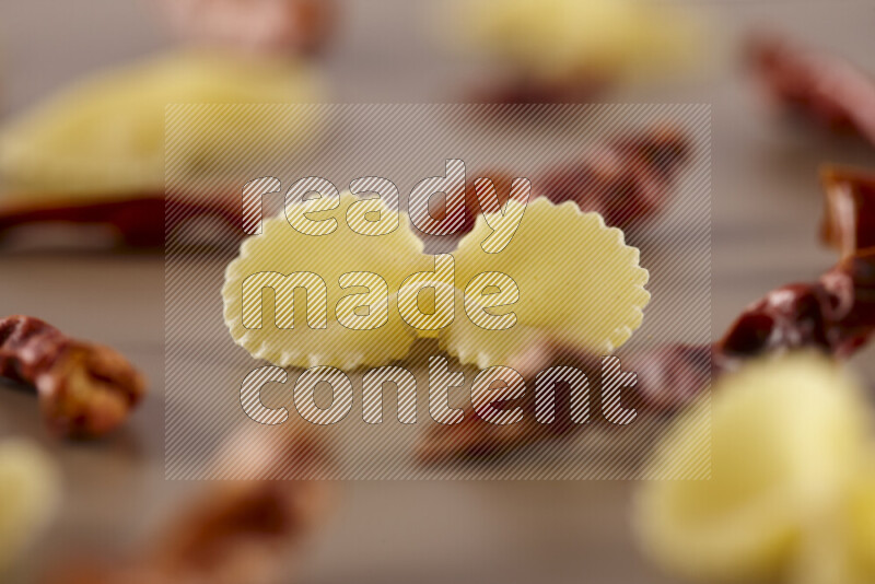 Raw pasta with different ingredients such as cherry tomatoes, garlic, onions, red chilis, black pepper, white pepper, bay laurel leaves, rosemary and cardamom on beige background