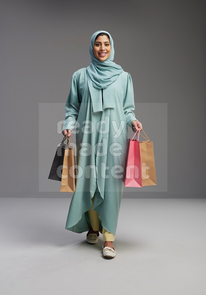 Saudi Woman wearing Abaya standing holding shopping bag on Gray background