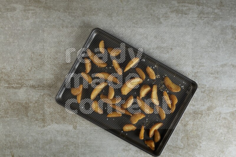 wedges potato in a black stainless steel rectangle tray on grey textured counter top