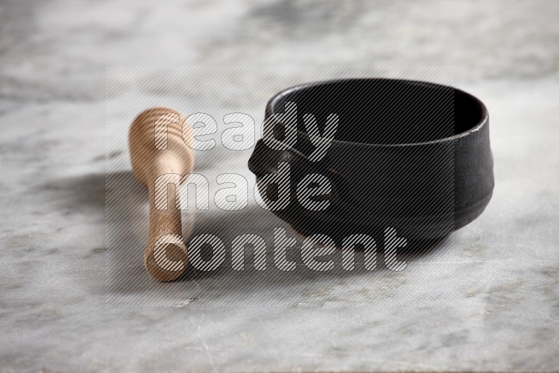 Black Pottery Bowl with wooden honey handle on the side with grey marble flooring, 15 degree angle