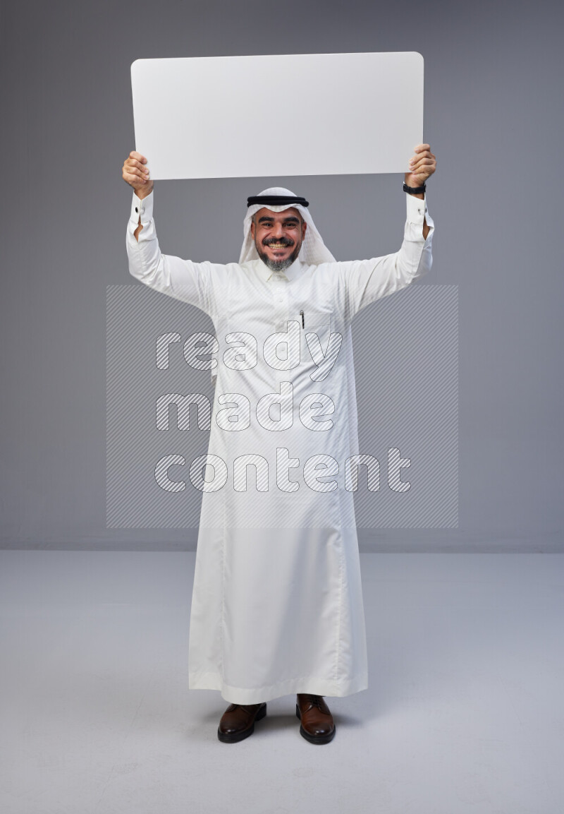 Saudi man Wearing Thob and white Shomag standing holding board on Gray background
