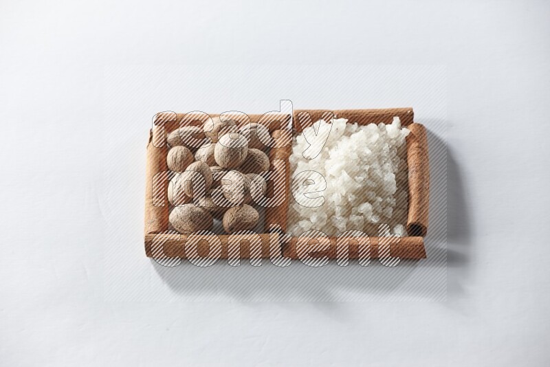 مربعان من أعواد القرفة ممتلئان بالملح الأبيض وجوزة الطيب علي خلفية بيضاء