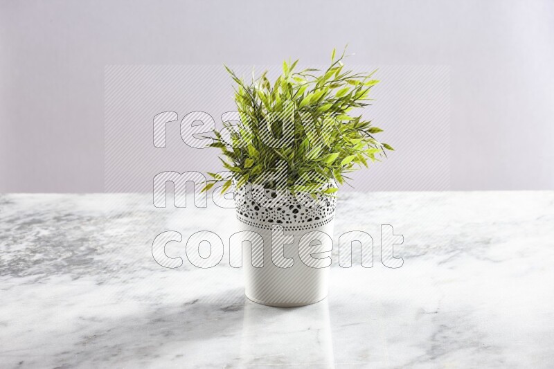 Green artificial plant in white decorative pot on grey marble background