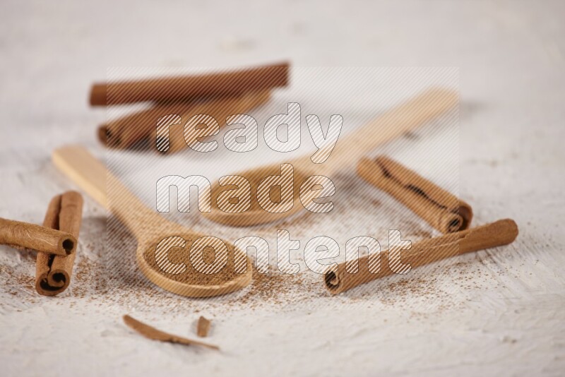 Two wooden spoons full of cinnamon powder with cinnamon sticks on white background