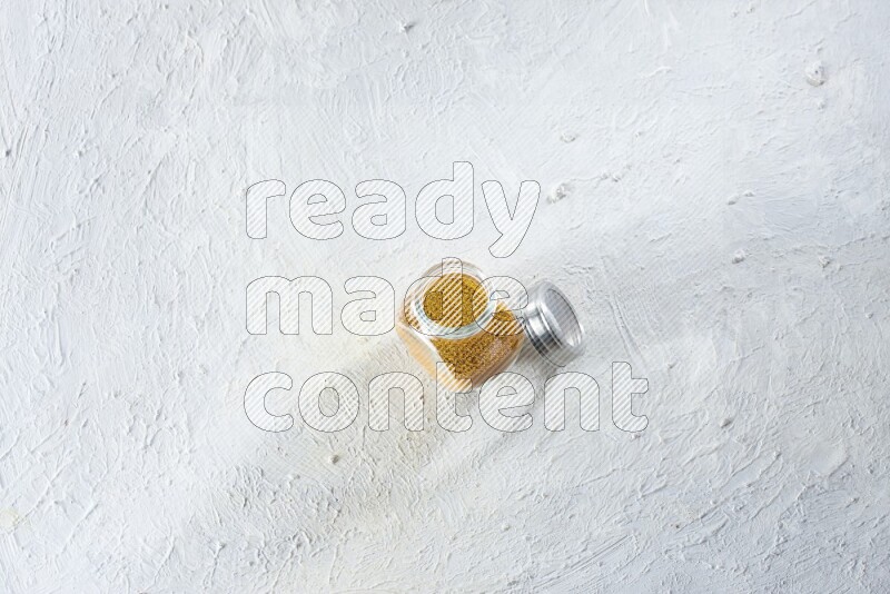 A glass spice jar full of turmeric powder on a textured white flooring