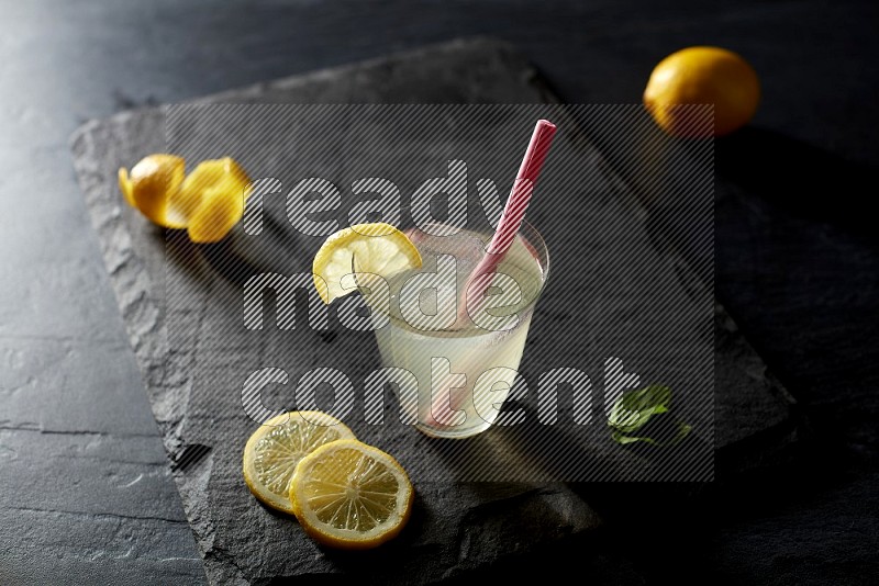 A glass of lemon juice with a straw on black background