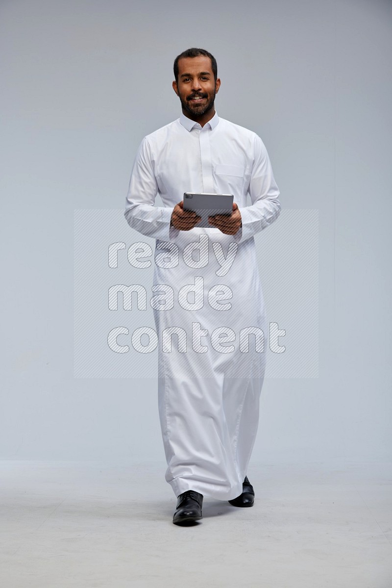 Saudi man wearing Thob standing working on tablet on Gray background