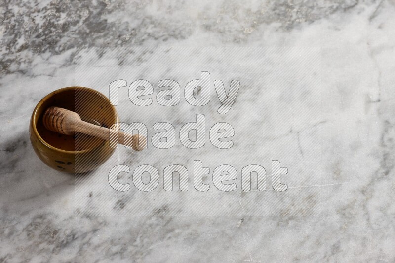 Multicolored pottery bowl with wooden honey dipper in it on grey marble background