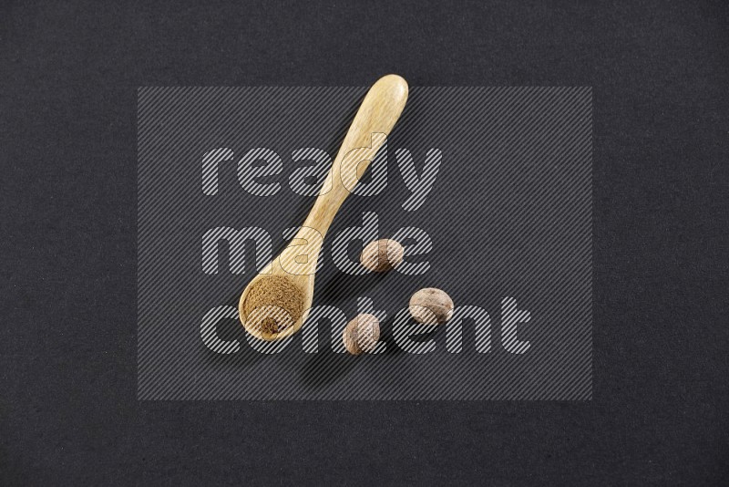 A wooden spoon full of nutmeg powder with nutmeg seeds beside it on a black flooring in different angles