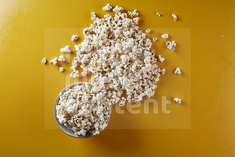 A white pottery bowl full of popcorn with popcorn beside it on a yellow background in different angles