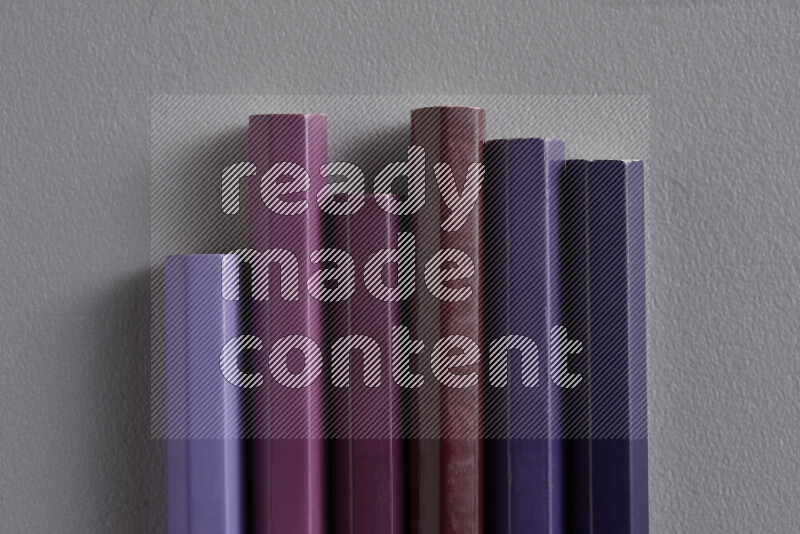 A collection of colored pencils arranged showcasing a gradient of purple hues on grey background