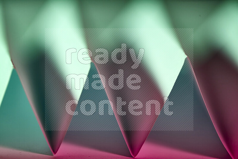 A close-up abstract image showing sharp geometric paper folds in green and pink gradients