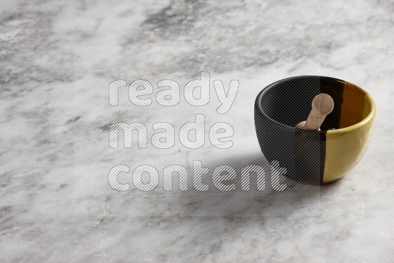 Multicolored pottery bowl with wooden honey dipper in it on grey marble background