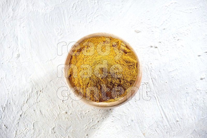 A wooden bowl full of turmeric powder on a textured white flooring