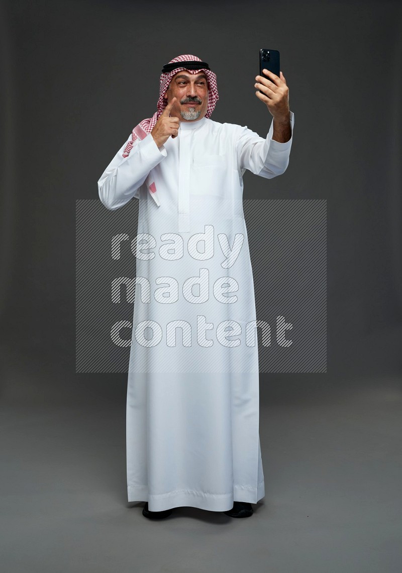 Saudi man with shomag Standing taking selfie on gray background