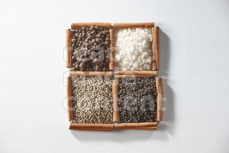 4 مربعات من أعواد القرفة ممتلئة ببهار الفلفل الحلو والملح الأبيض والفلفل الأبيض والفلفل الأسود على أرضية بيضاء