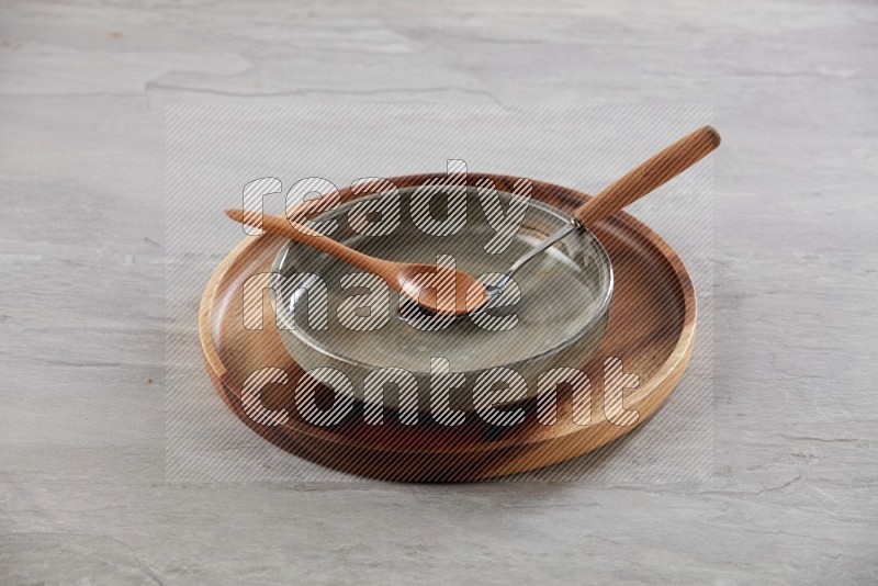 multi color pottery round dish on top of brown wood round plate and spoon, on grey textured countertop