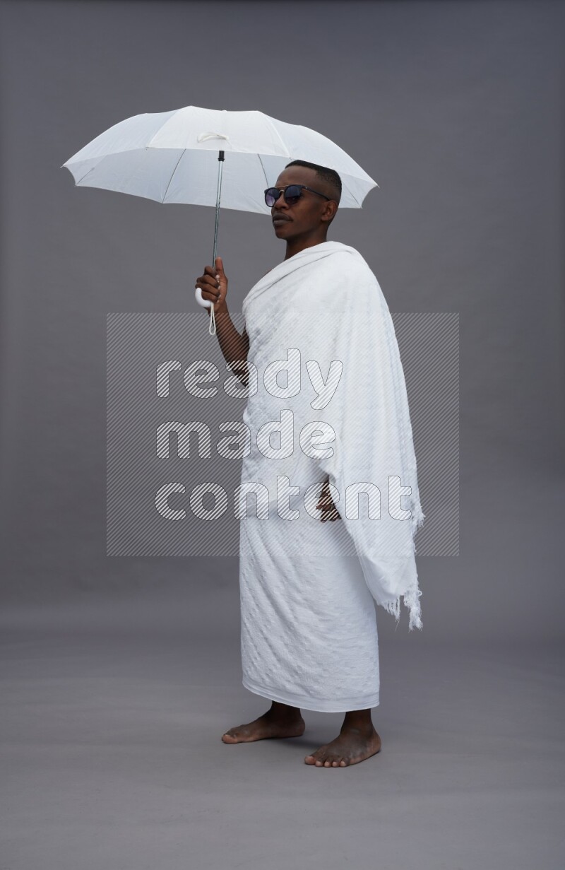 A man wearing Ehram Standing holding umbrella on gray background