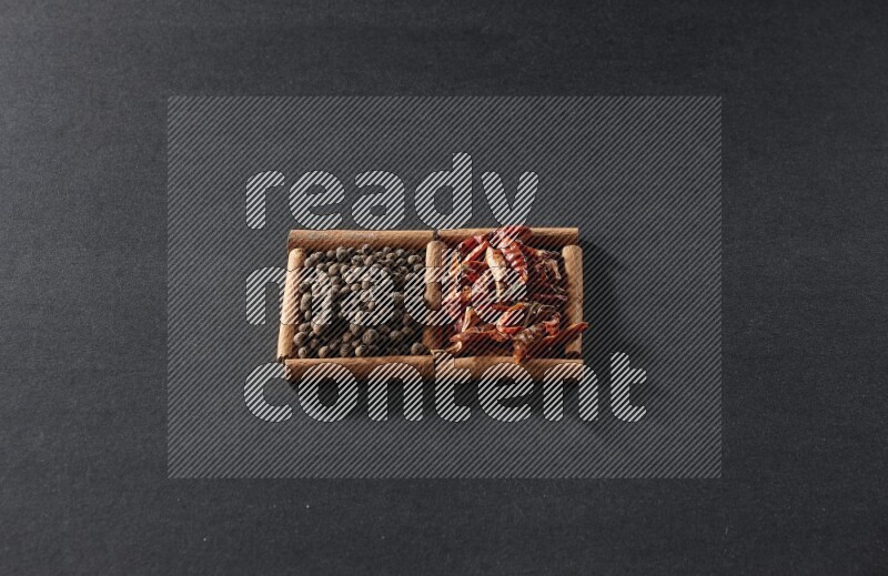 مربعان من أعواد القرفة ممتلئان بالفلفل الحار المجفف وحبوب بهار الفلفل الحلو علي خلفية سوداء