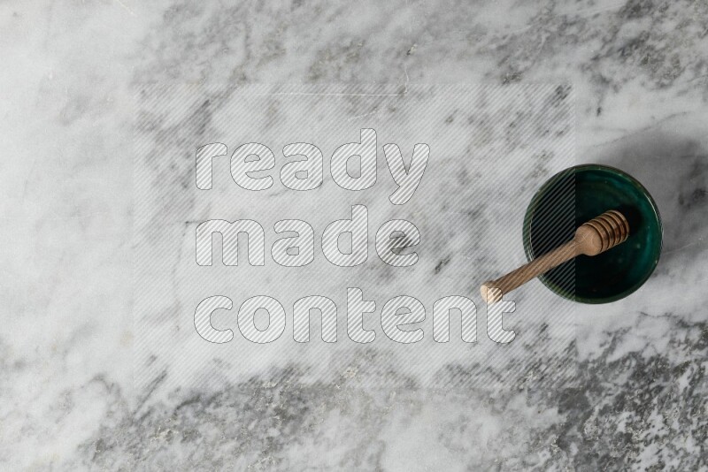 Dark green pottery bowl with wooden honey dipper in it on grey marble background