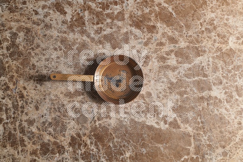 Top View Shot Of A Small Copper pan On beige Marble Flooring