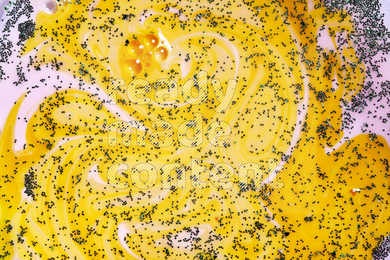 A close-up of sparkling green glitter scattered on swirling yellow and pink background