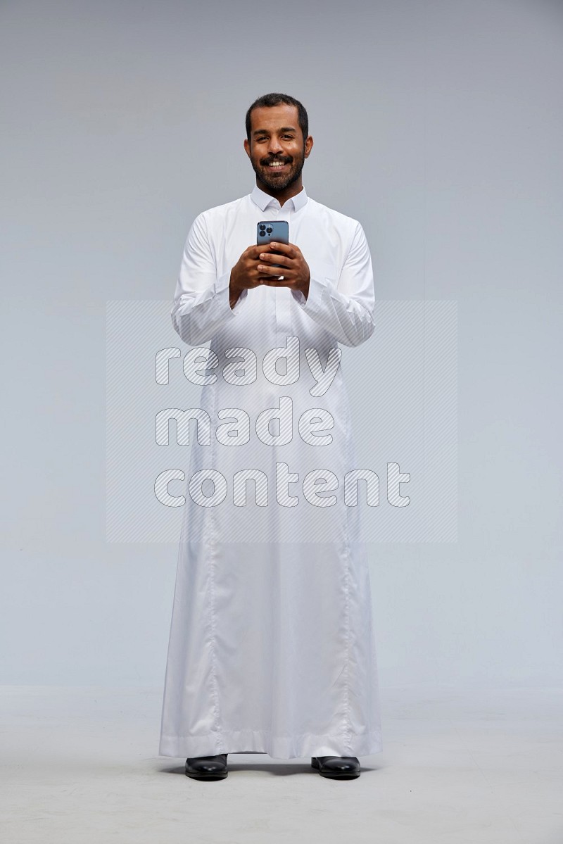 Saudi man wearing Thob standing texting on phone on Gray background
